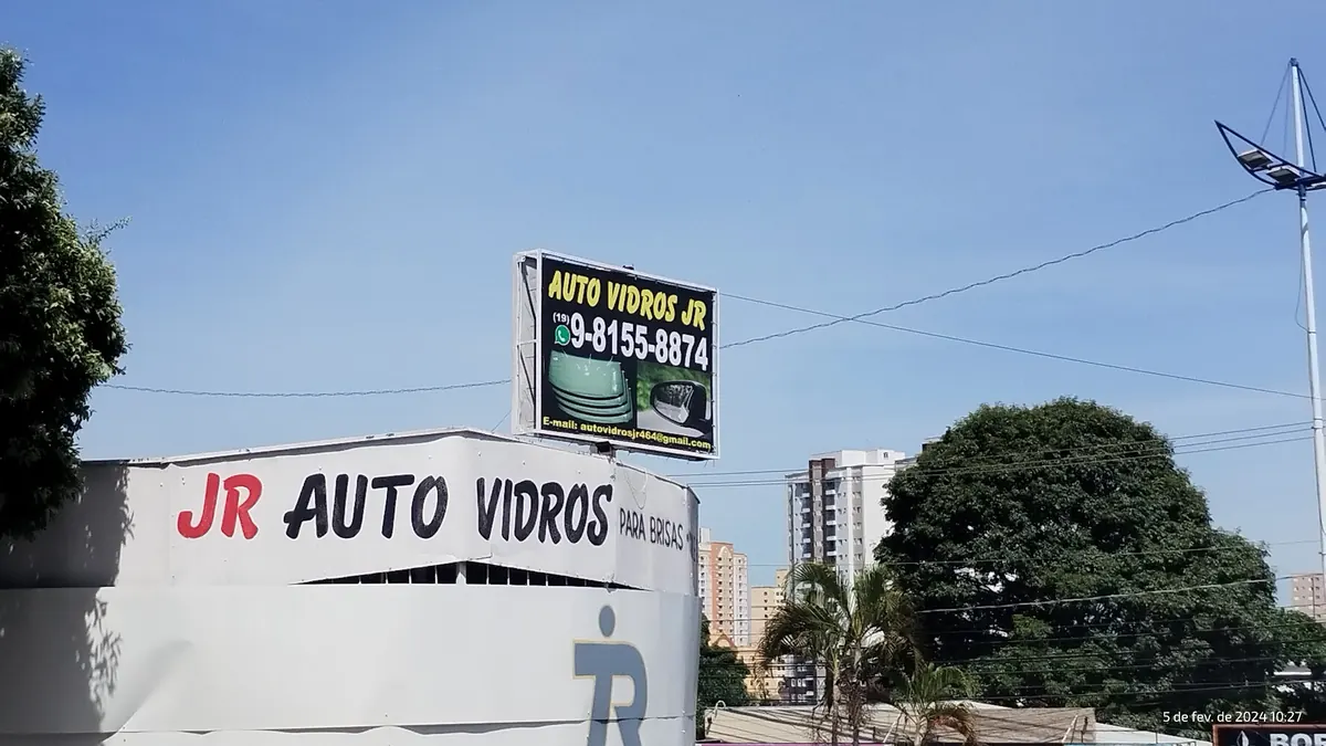 Fachada da JR Auto Vidros com a faixa JR Auto Vidros e o painel com o telefone